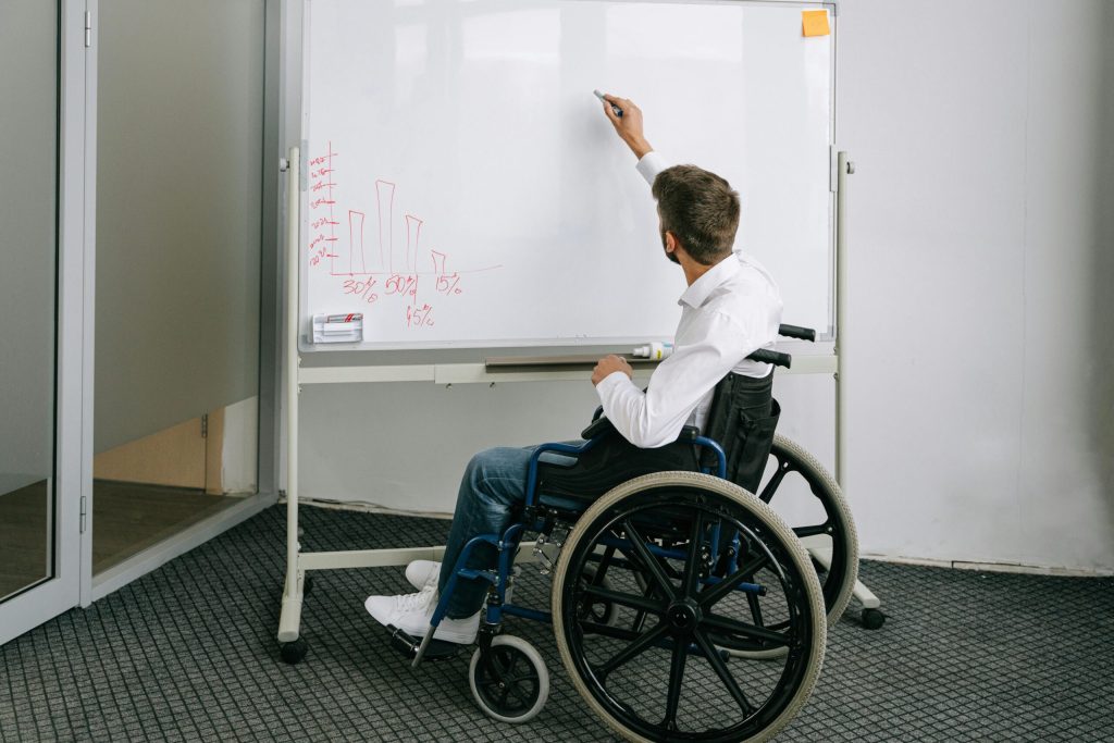 Person in a wheelchair writing on a whiteboard during a collaborative meeting